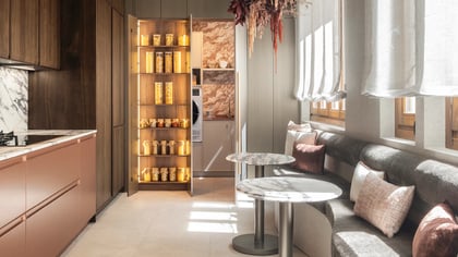 Cocina y comedor modernos con gabinetes de madera y cobre, encimeras de mármol y una acogedora área de asientos con mesas redondas.