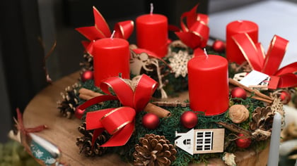 Festlicher Adventskranz mit vier roten Kerzen, roten Bändern, Tannenzapfen und Naturdekorationen.