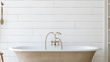 Una bañera exenta color crema con grifería de latón vintage en un baño luminoso y sereno.