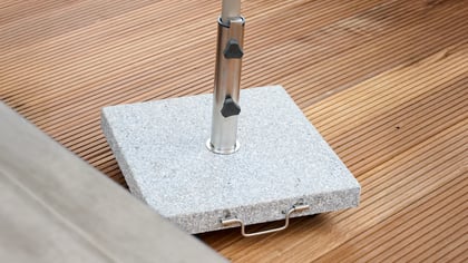 Nahaufnahme eines Sonnenschirmständers aus Granit auf einem Holzdeck, der Stabilität und Eleganz für Außenbereiche bietet.
