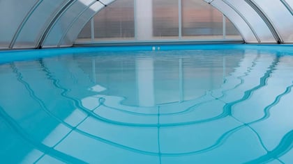 Piscina cubierta con agua azul clara y un cerramiento transparente arqueado.