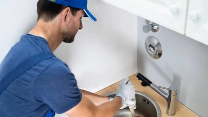 Un fontanero con uniforme azul repara un fregadero de cocina.