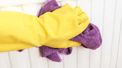 Mano con guante de goma amarillo sosteniendo un paño de microfibra morado, limpiando una superficie.