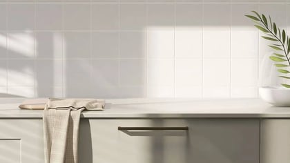 Encimera de cocina moderna gris claro con armarios taupe y tiradores de bronce, con platos apilados, un paño a cuadros y una planta en un jarrón.