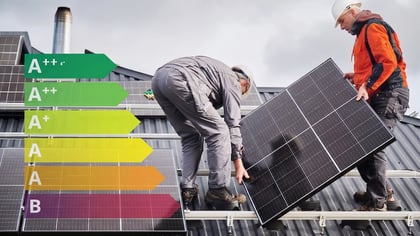 Trabajadores instalan paneles solares negros en un tejado, con una escala de eficiencia energética (A+++ a B) superpuesta, promoviendo energía renovable.