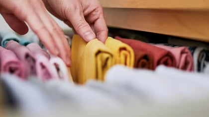 Una mano organiza ropa colorida y bien doblada verticalmente en un cajón de madera.