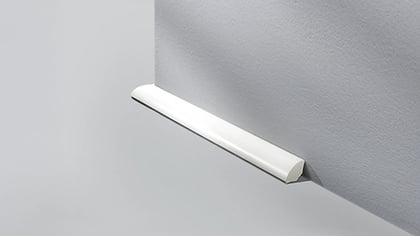 Nahaufnahme einer weißen Viertelkreisleiste, die an einer grauen Wand befestigt ist und einen sauberen Übergang zwischen Wand und Boden bildet.