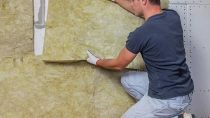 Hombre con guantes instalando aislamiento térmico amarillento en una pared.