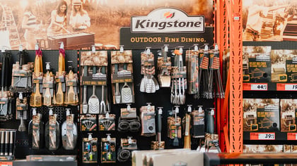 Kingstone Grillzubehör und Werkzeuge in einem Verkaufsregal, darunter Grillbürsten, Werkzeugsets, Abdeckungen und Räucherbedarf.