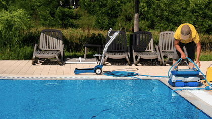 Eine Person bereitet einen blauen Poolroboter am Rand eines Schwimmbeckens vor.