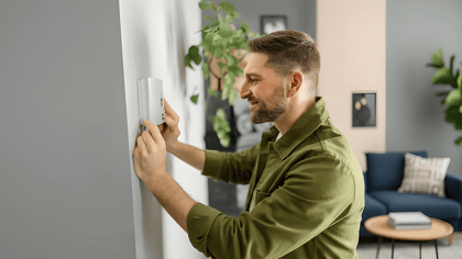 Ein Mann befestigt eine intelligente Thermostatbasis an einer grauen Wand, um ein modernes Temperaturregelungssystem in seinem Zuhause zu installieren.