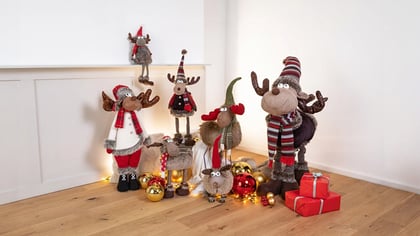 Verschiedene festliche Plüsch-Rentiere und Elche als Weihnachtsdekoration, mit Kugeln und Geschenken arrangiert.