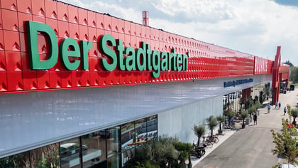 Großes modernes Geschäftshaus mit leuchtend roter Fassade und grünem „Der Stadtgarten“-Schriftzug.
