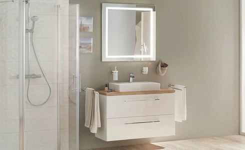 Modernes Badezimmer mit weißem Waschtisch mit Holzplatte, beleuchtetem Spiegel und Glasduschkabine.