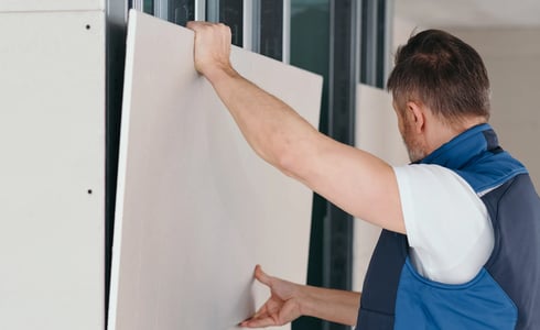 Arbeiter montiert eine helle Trockenbauplatte auf eine Metallständerwand.