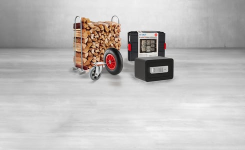 Sortiment an Eisenwaren: ein Metall-Brennholzwagen mit Holzscheiten, rotes Rad, Lenkrolle, schwarzer Werkzeugkasten und digitaler Safe.
