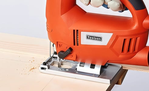Nahaufnahme einer orangefarbenen Toolson Stichsäge, die ein Holzstück schneidet, wobei der Fokus auf Präzision und der Marke liegt.