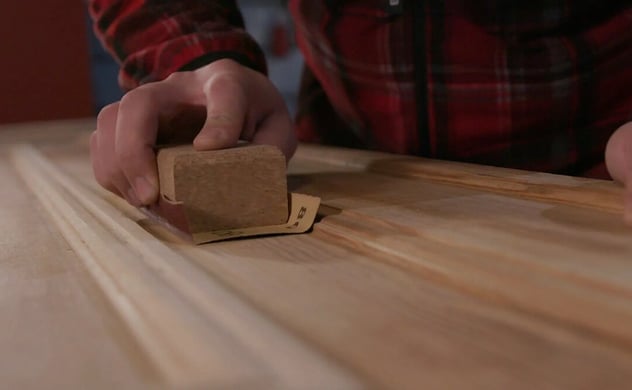 Mann schleift mit einem Schleifpapier und einem Schleifklotz ein Holzbrett ab