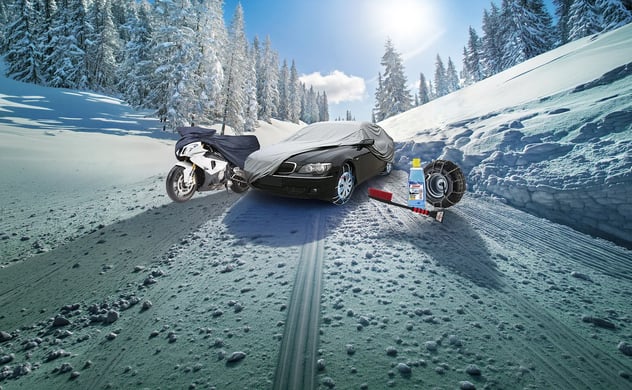 Zugedecktes Auto und Motorrad auf schneebedeckter Straße mit Winterzubehör: Schneeketten, Reinigungsflüssigkeit und Bürste.