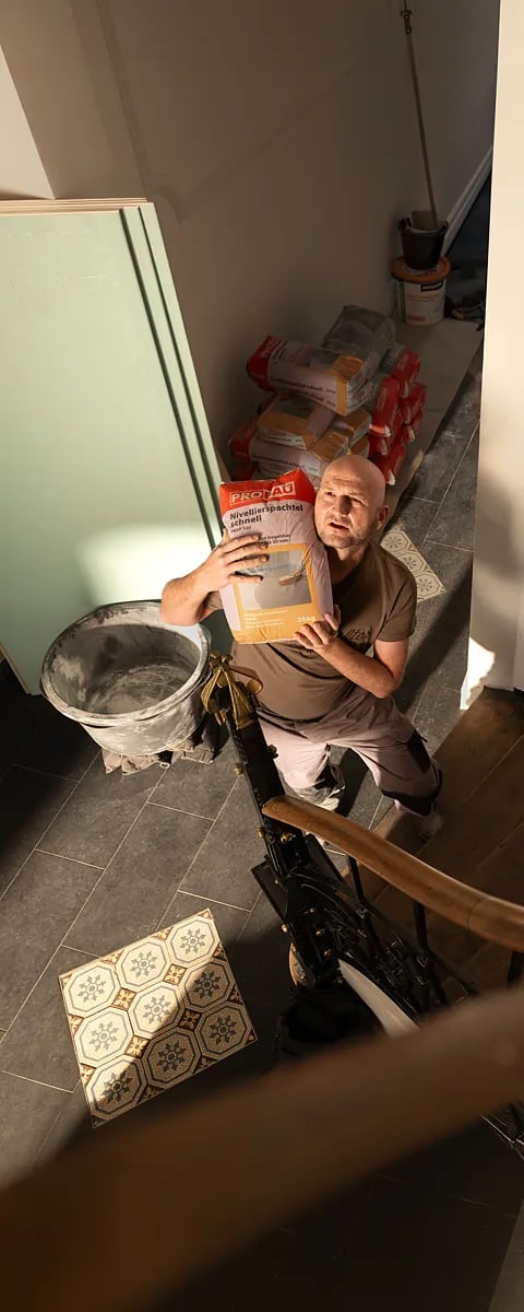 Mann hält einen 20kg Sack orange-weißen Nivellierspachtel in einer Renovierungsumgebung.