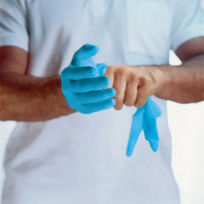 Einmalhandschuhe u-fit - XL, Kunststoff - Eine Person mit einem weißen T-Shirt, die blaue medizinische Handschuhe anzieht, um sich vor Keimen und Viren zu schützen.