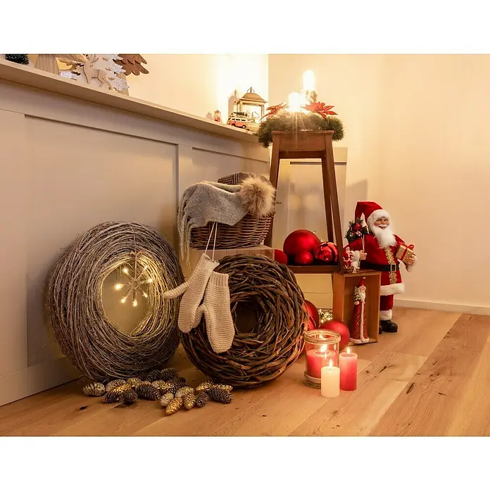 Weihnachtsmann mit Geschenk und Tanne - Höhe: 60 cm, Rot, Weiß, Mit Tannenausschnitt - Festliche Weihnachtsdekoration mit Kränzen, Kerzen und Weihnachtsmannfiguren auf einem Holzboden.