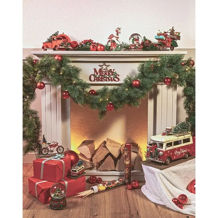 Dekofigur Weihnachtsbus - L x B x H: 39 x 18 x 27 cm, Metall, X-Mas - Weihnachtliche Dekoration mit einer Girlande, roten Kugeln und Spielzeugautos vor einem Kamin.
