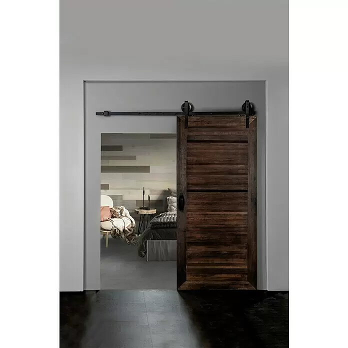 Indo Holzschiebetür Barn Door Semi Solid - 100 x 215 cm, Shorea, Parma - Rustikale dunkle Holzschiebetür mit schwarzer Beschlag, teilweise geöffnet, um ein Schlafzimmer zu zeigen.