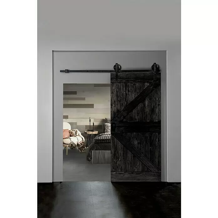 Indo Holzschiebetür Barn Door Colored - 100 x 215 cm, Teak, Charred - Dunkle Holzscheunentür mit schwarzem Metall-Schiebesystem, die ein modernes Schlafzimmer teilweise offenbart.