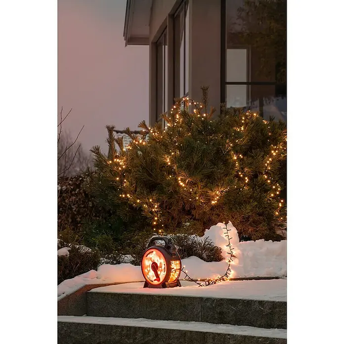 Konstsmide LED-Lichterkette Compactlights - Außen, Lichtfarbe: Bernstein, Anzahl Leuchtmittel: 600 Stk., Netzbetrieben, 13,18 m - Winterliche Gartenszene mit beleuchtetem Heizstrahler und Lichterkette auf einer verschneiten Treppe vor einem Haus.
