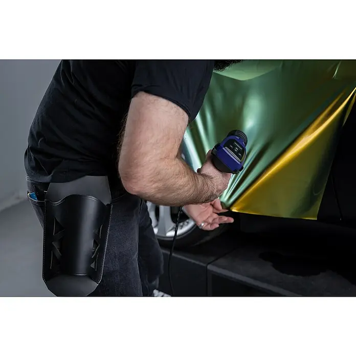 Weldy Heißluftgebläse HG 530-A Car-Wrap-Kit - 2.300 W, Temperaturbereich: 80 °C - 650 °C - Ein Mann appliziert mit einer Heißluftpistole eine glänzend goldene Folie auf ein Fahrzeug, wobei er sorgfältig auf eine faltenfreie Oberfläche achtet.