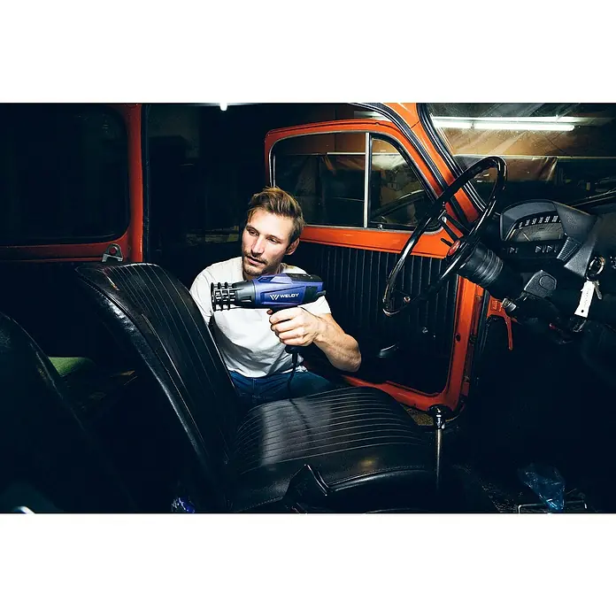 Weldy Heißluftgebläse HG 530-A Car-Wrap-Kit - 2.300 W, Temperaturbereich: 80 °C - 650 °C - Ein Mann benutzt eine Weldy Heißluftpistole, um an einem Oldtimer-Autositz zu arbeiten und diesen zu restaurieren. Ideal für Profis und Hobbybastler.