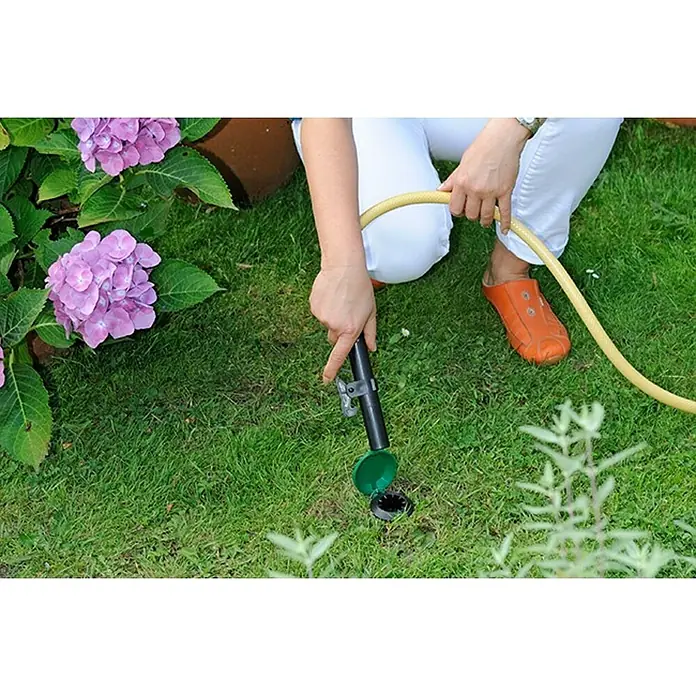 Wassersteckdose - 1″ - Eine Person schließt einen Schlauch an eine unterirdische Bewässerungsanlage in einem grünen Garten an.