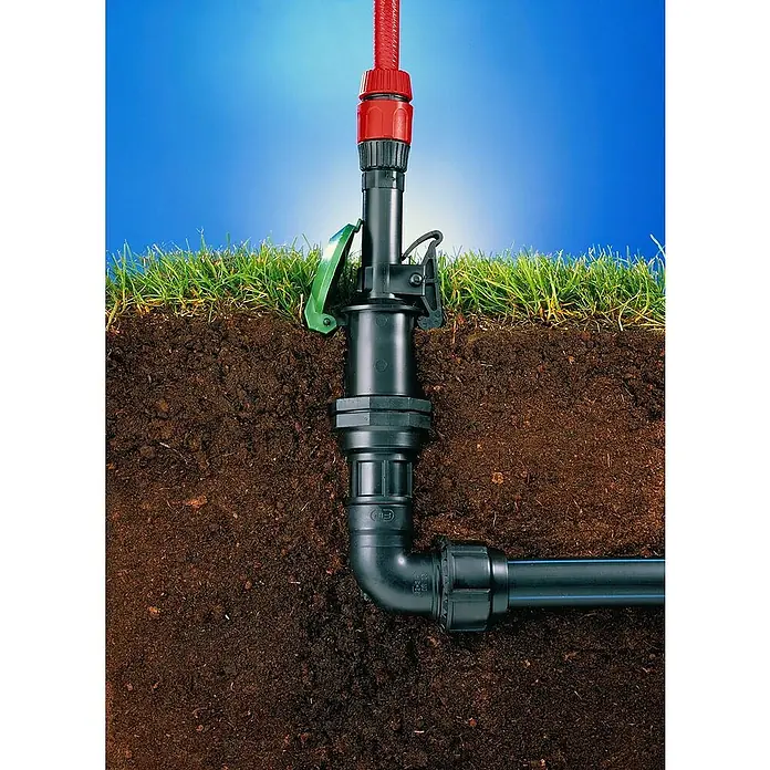 Wassersteckdose - 1″ - Nahaufnahme einer Bewässerungsinstallation im Gartenboden mit einem roten Schlauchanschluss, der für die Bewässerung von Pflanzen verwendet wird.
