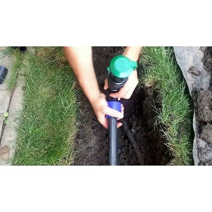 Wassersteckdose - 1″ - Eine Person installiert einen Bewässerungsregner in einem Garten, wobei die grüne Kappe und die blaue Verbindung hervorstechen.