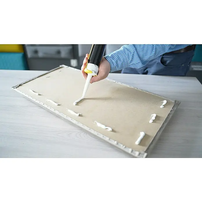 Fllow Set de paneles de pared acolchados Set Inari A1 - 270 x 150 cm, Taupe - Un artesano aplica adhesivo a una tabla de madera con una pistola de cartucho para un proyecto de bricolaje.