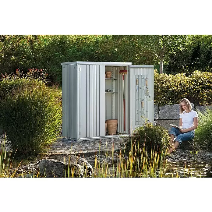 Biohort Geräteschrank 150 - Silber Metallic - Silberner Metall-Gartenschrank in einem grünen Garten, mit Regalen, Werkzeugen und Töpfen.