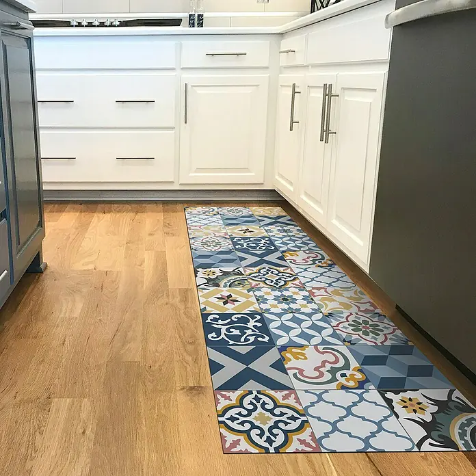 Alfombra de vinilo Artdeco Patch - Azul, 140 x 80 cm - Una vista de la cocina con un pasillo decorativo delante de los armarios de cocina blancos en un suelo de madera clara.