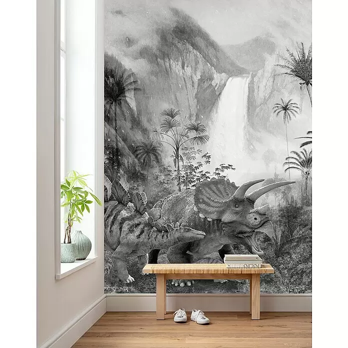Komar Fototapete Jurassic Waterfall - B x H: 200 x 280 cm, Vlies - Schwarz-weißes Dinosaurier-Wandbild in einem Raum mit Holzbank und Pflanze, das seine Größe zeigt.