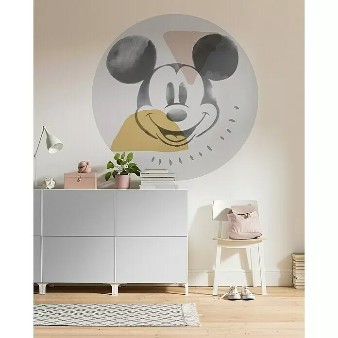 Komar Fototapete rund Mickey Abstract - 128 cm, Selbstklebend - Ein hellgrauer viertüriger Aufbewahrungsschrank, mit Deko versehen, in einem Raum mit einem großen Mickey-Maus-Wandbild für eine spielerische Einrichtung.