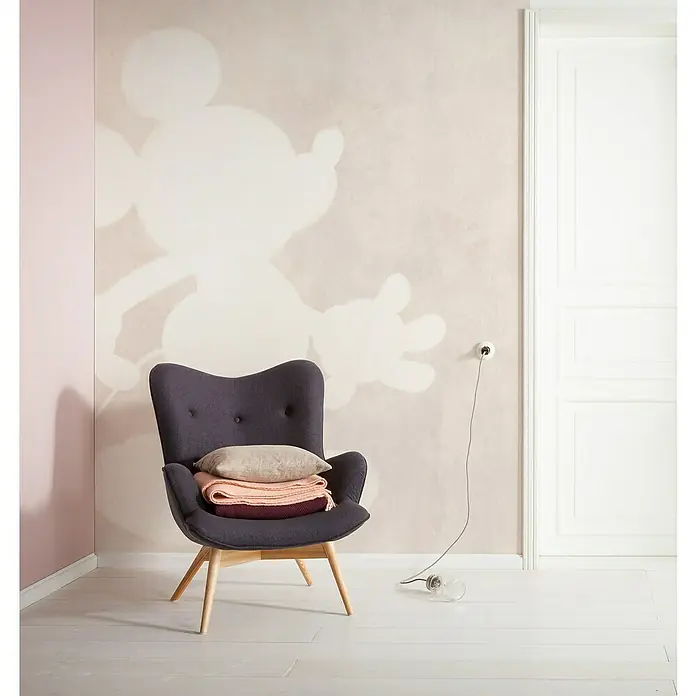 Komar Fototapete Mickey Contour - B x H: 200 x 280 cm, Vlies - Elegantes Interieur mit einem dunkelgrauen Sessel auf Holzbeinen, dekoriert mit Kissen und Decken, vor einer Wand mit Mickey-Mouse-Motiv.