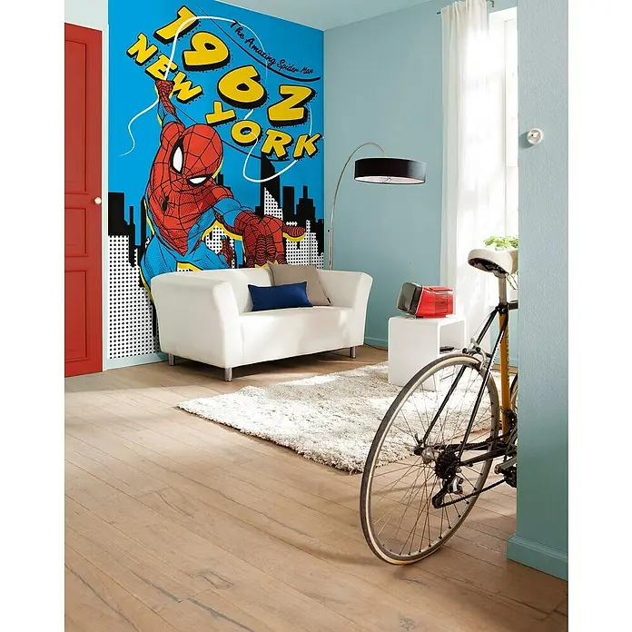 Komar Fototapete Spiderman 1962 - B x H: 200 x 280 cm, Vlies - Ein Zimmer mit einem Spider-Man-Wandbild, einem weißen Sofa, einem Teppich und einem Fahrrad. Das Wandbild zeigt Spider-Man in New York.