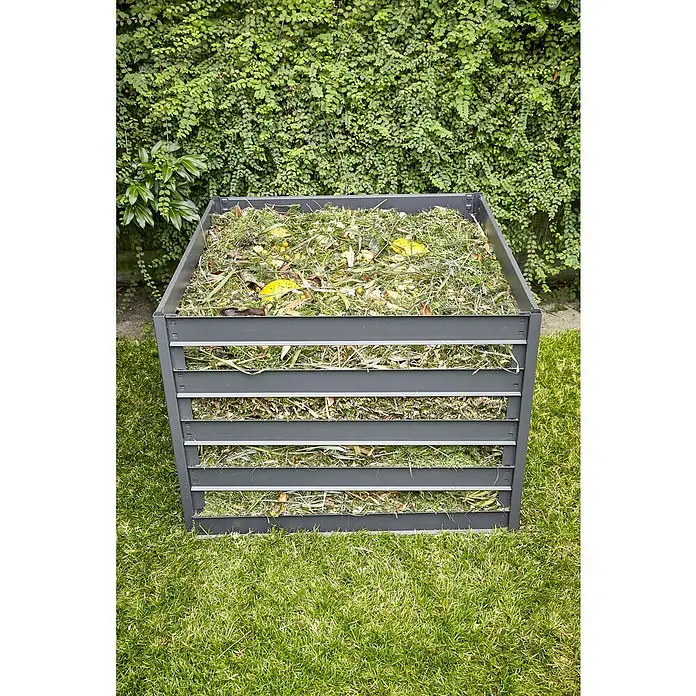 Gardol Komposter - 600 l, 93 x 93 x 70 cm - Ein quadratischer, grauer Kompostbehälter aus Latten steht im Garten, gefüllt mit Gartenabfällen. Im Hintergrund grünt eine Hecke.