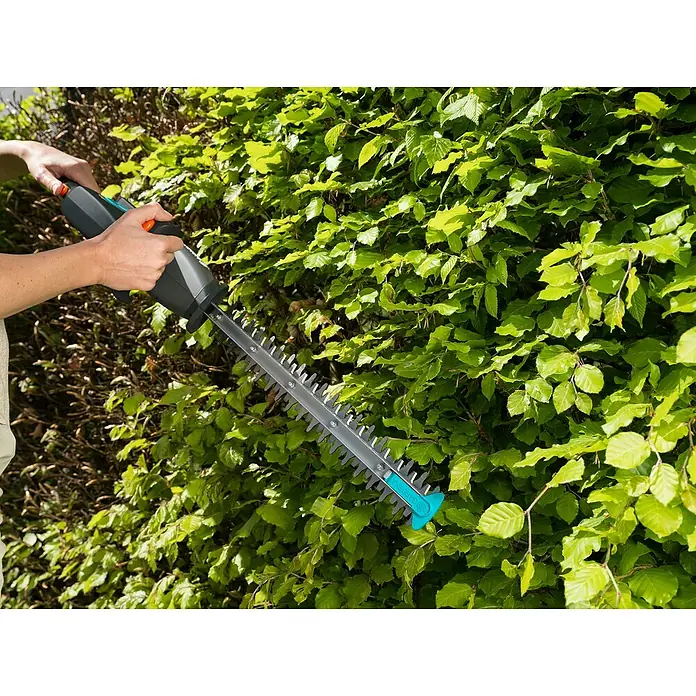 Gardena EasyCut Akku-Heckenschere - 14,4 V, Li-Ionen, 2 Ah, 1 Akku - Eine Person benutzt eine Gardena Akku-Heckenschere, um eine grüne Hecke zu schneiden. Das Gerät ist ein nützliches Werkzeug für die Gartenarbeit.