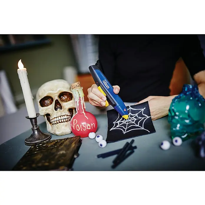 Rapid Heißklebepistole EG - Blau, Gelb, Durchmesser Klebepatrone: 7 mm - Halloween-Dekoration mit einer Klebepistole. Eine Person benutzt eine Rapid Klebepistole, um ein Spinnennetz auf ein schwarzes Stück Stoff zu zeichnen.