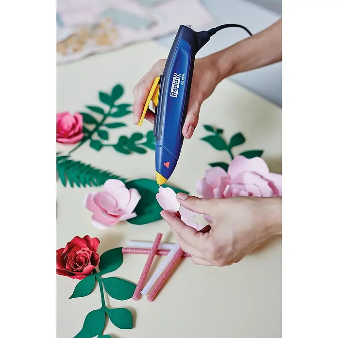 Rapid Pistola termoencoladora EG Pen - Diámetro cartucho de cola: 7 mm - Primer plano de una persona haciendo flores de papel con una pistola de pegamento Rapid EG Pen. Hay material de manualidades esparcido sobre una mesa.