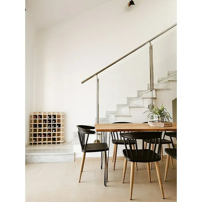 Astigarraga Weinregal - L x B x H: 75 x 22 x 75 cm, Anzahl Flaschen: 36 Stk. - Ein Weinregal aus hellem Holz steht neben einer Treppe in einem hellen Raum, ergänzt durch einen Esstisch mit Stühlen.