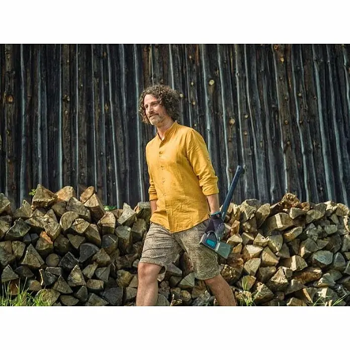 Gardena Gartenhandschuhe Geräte - 10, XL, Grau/Türkis, Polyester - Ein Mann mit einer Axt vor einem Holzhaufen, bereit für die Arbeit. Die Axt ist ein robustes Werkzeug für Holzarbeiten im Freien.
