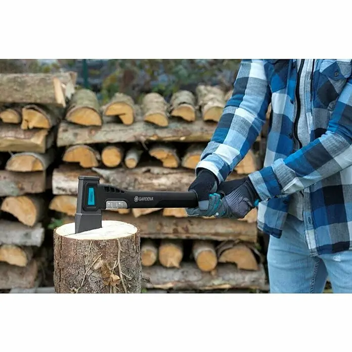 Gardena Gartenhandschuhe Geräte - 10, XL, Grau/Türkis, Polyester - Eine Gardena Axt steckt in einem Holzscheit, während eine Person im Hintergrund vor einem Holzstapel steht.