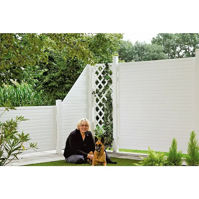 T & J Lightline Sichtschutzelement - 90 x 180 cm, Abgeschrägt, Weiß - Eine Frau sitzt mit ihrem Hund vor einem weißen Sichtschutzzaun mit Latten und Rankgitter, umgeben von üppigem Grün.